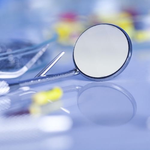 Gros plan sur un miroir dentaire en acier inoxydable posé sur une surface réfléchissante bleue, avec d'autres instruments dentaires flous en arrière-plan.